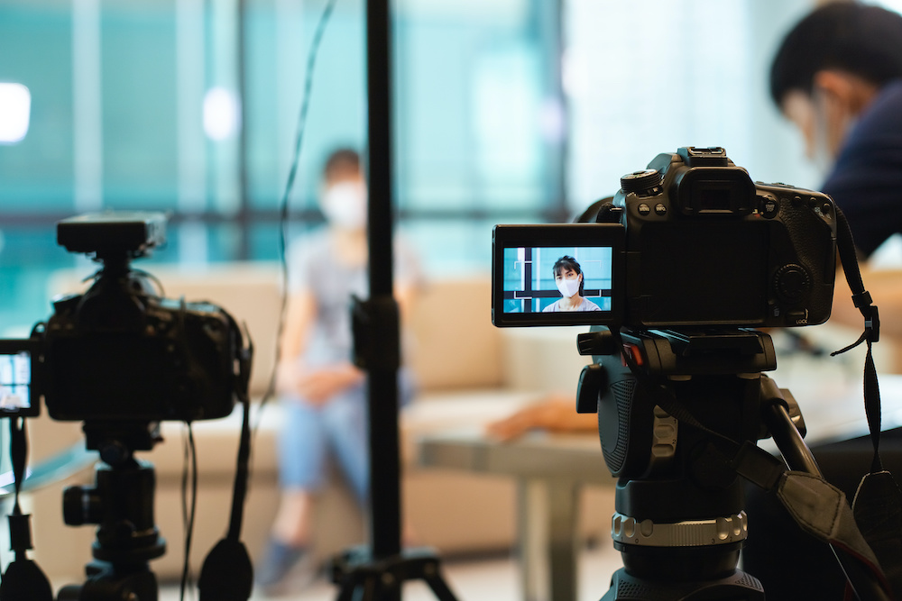 close up camera on tripod recording video blog in studio filming with asian young woman wearing face mask protection in display screen.